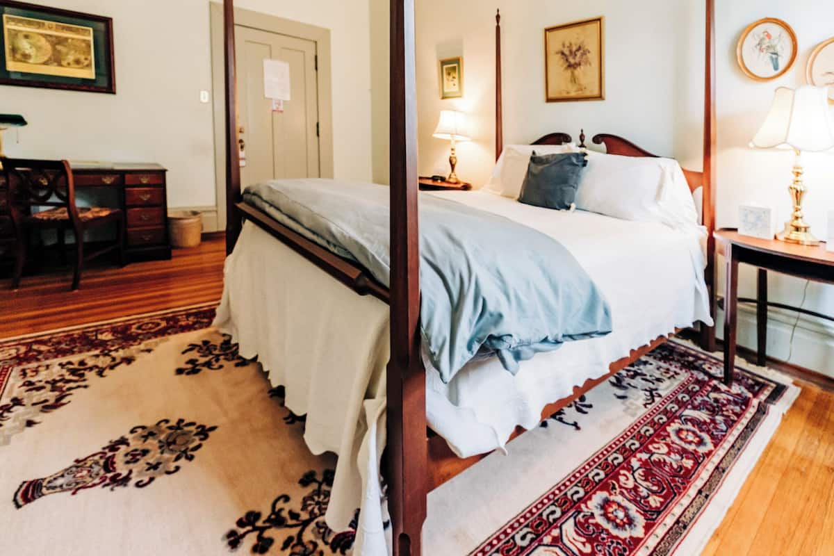 A bedroom with a four-poster bed, a desk, and a chair.