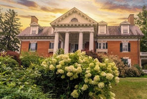 A large brick building with a symmetrical facade, central entrance with columns, and a well-maintained garden with hydrangea bushes. - The Mercersburg Inn (Mercersburg)