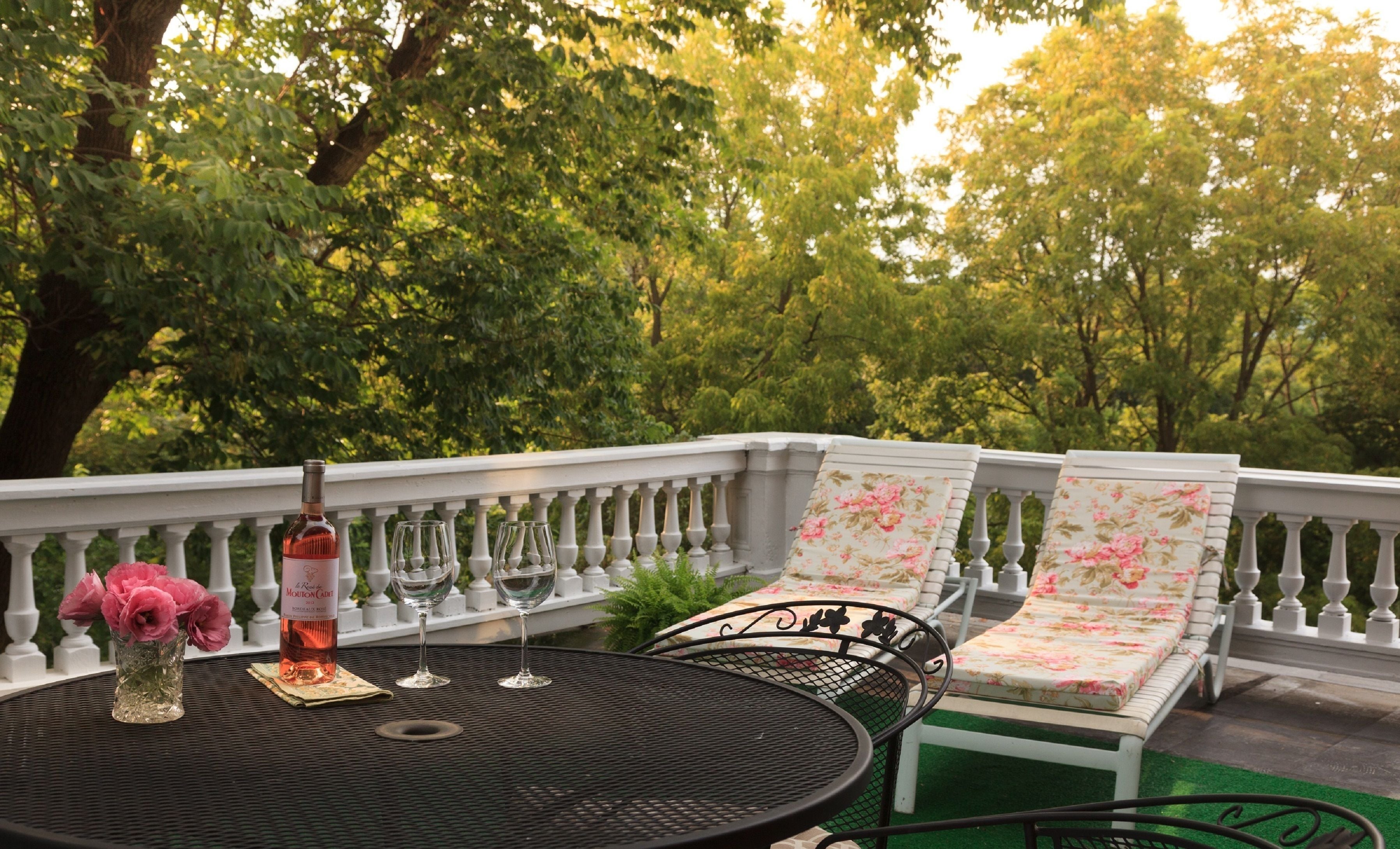 A balcony with a round table, two lounge chairs, a bottle of wine, and wine glasses.