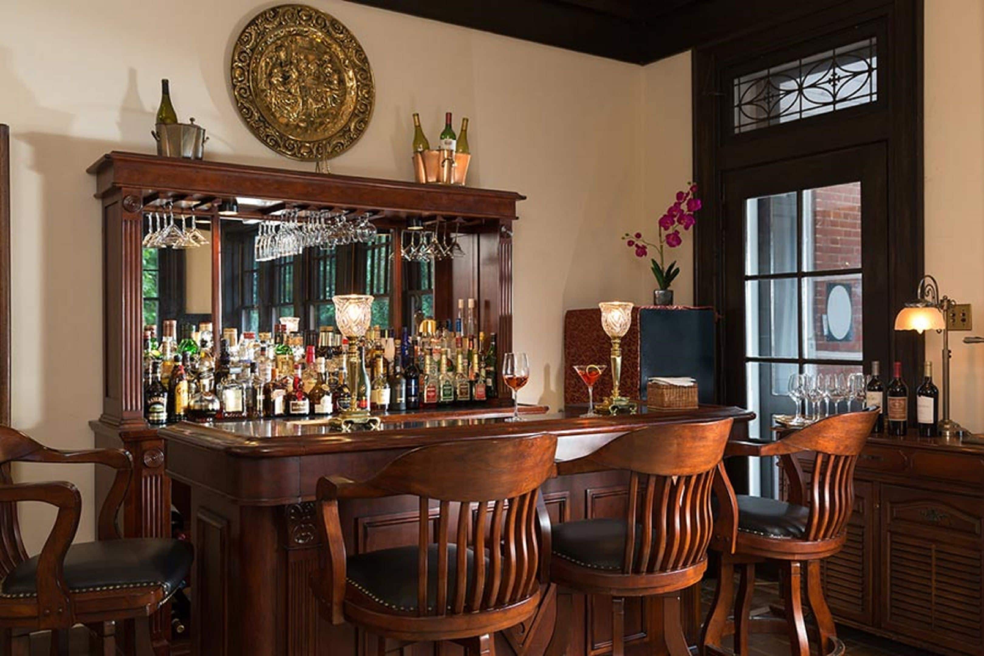 A bar area with a wooden bar counter, multiple bottles, and a large mirror.