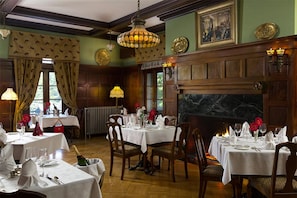 A dining room with multiple tables set for a meal, a fireplace, and a chandelier. - The Mercersburg Inn (Mercersburg)
