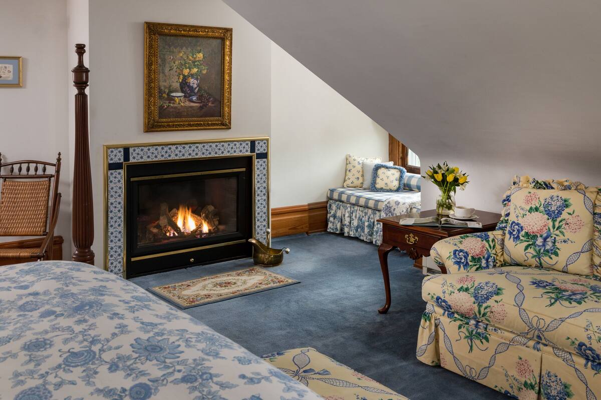A cozy room with a fireplace, a sofa, a chair, and a small table with a vase of flowers.