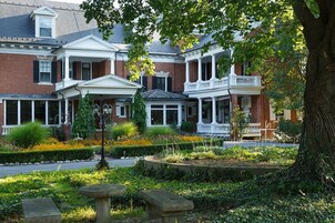 Una hilera de casas adosadas de ladrillo con detalles blancos, un porche cubierto y un jardín ajardinado con un banco de piedra.