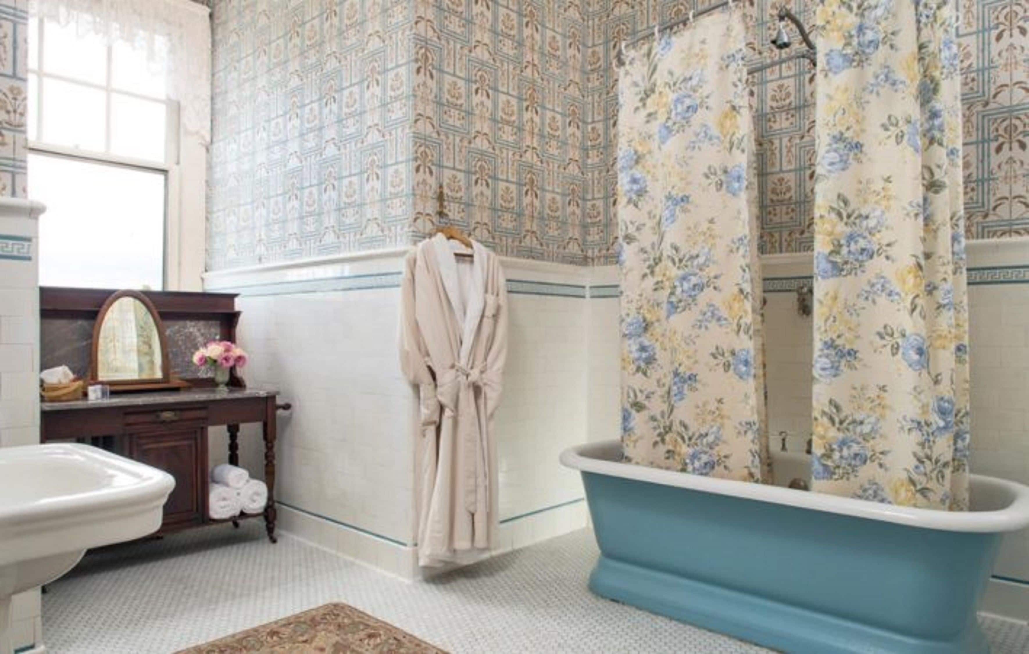 A bathroom with a clawfoot bathtub, a mirror, a vanity with a sink, and patterned wallpaper.