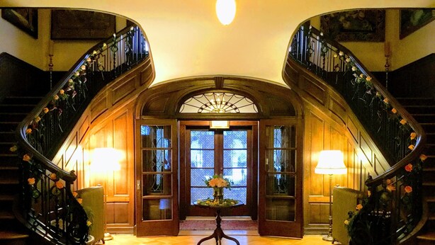 A grand staircase with ornate railings and a central chandelier, leading to a wooden door with glass panels. - The Mercersburg Inn (Mercersburg)