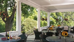 A covered outdoor patio with round tables and wicker chairs, surrounded by lush greenery and trees. - The Mercersburg Inn (Mercersburg)