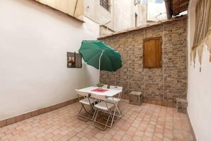 Un pequeño patio con una mesa y sillas, una sombrilla verde y un muro de ladrillo.