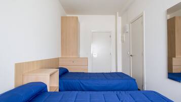A bedroom with two beds, a wooden desk, a wardrobe, and a mirror.