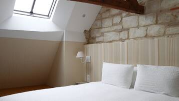 Ein Schlafzimmer mit schrägen Wänden, einem Oberlicht, einem Bett mit weißer Bettwäsche, einem Nachttisch und einer Wandlampe.