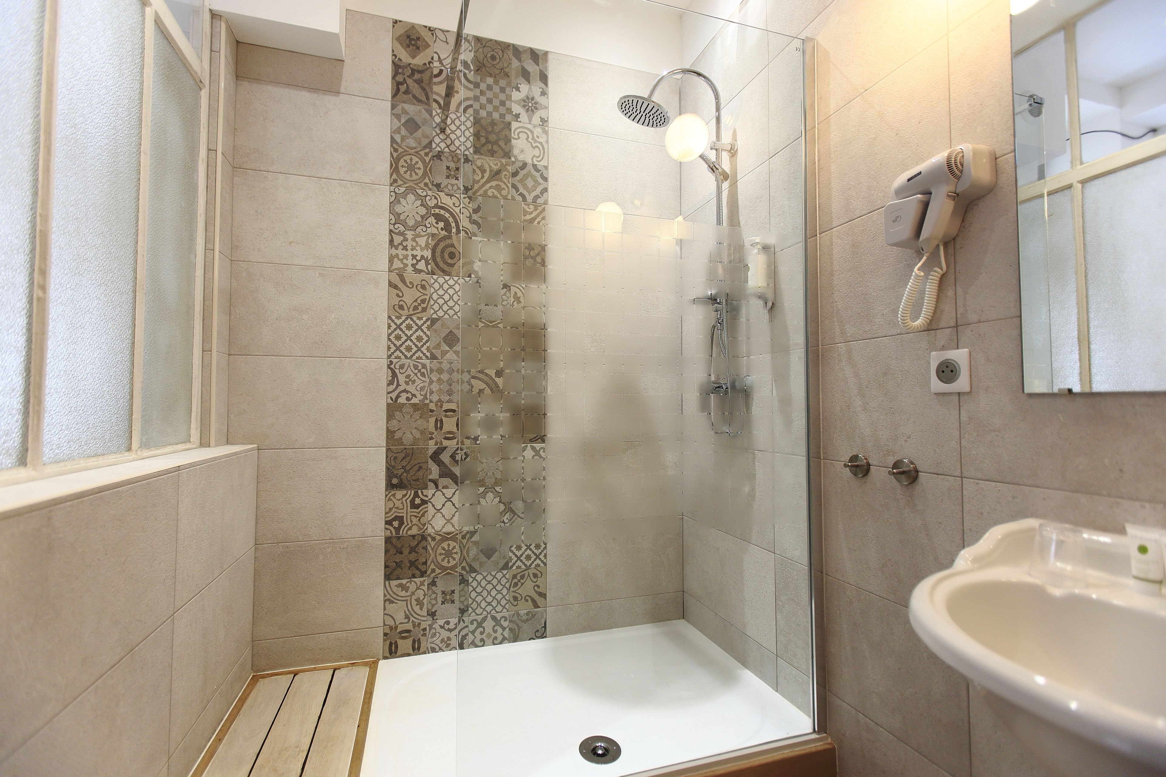 A shower with a glass door, a white sink, and a patterned tile wall.