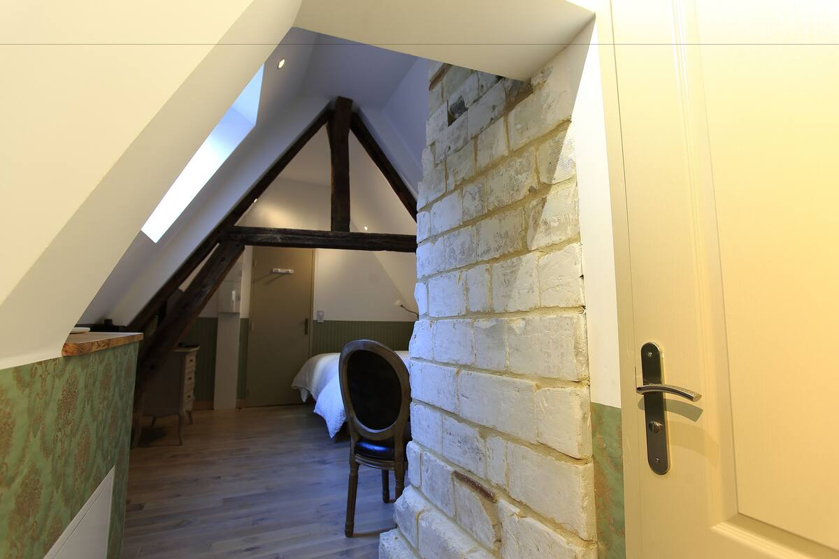 Een kamer met een schuine plafond, een houten stoel, een bed en een witte deur.