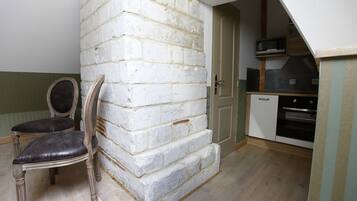 Ein Zimmer mit weißer Ziegelwand, einem hölzernen Stuhl mit schwarzem Kissen, einer Tür und einer Küchenzeile mit Mikrowelle und Backofen.