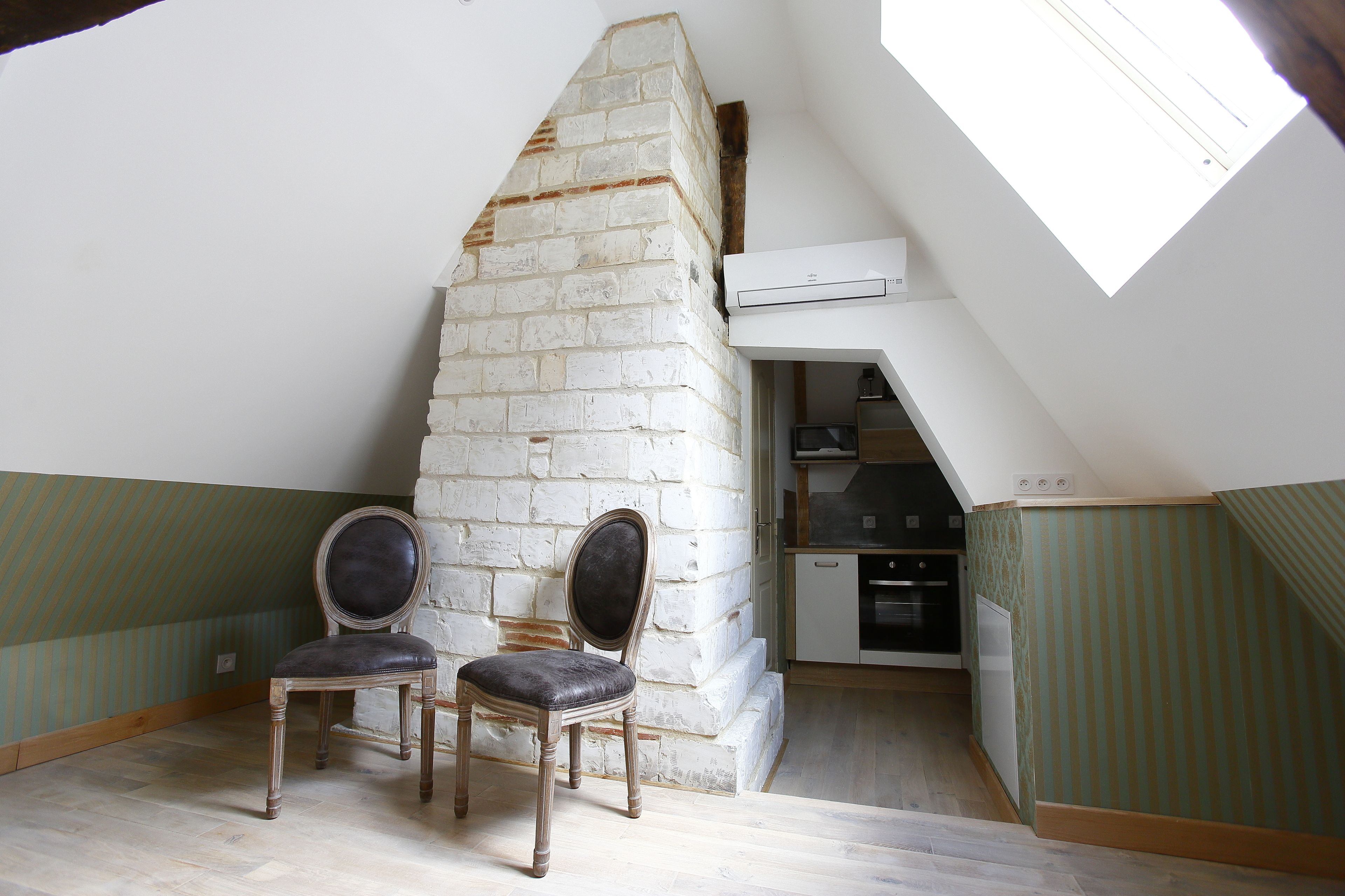 Una habitación con techo inclinado, pared de ladrillo y cocina integrada.