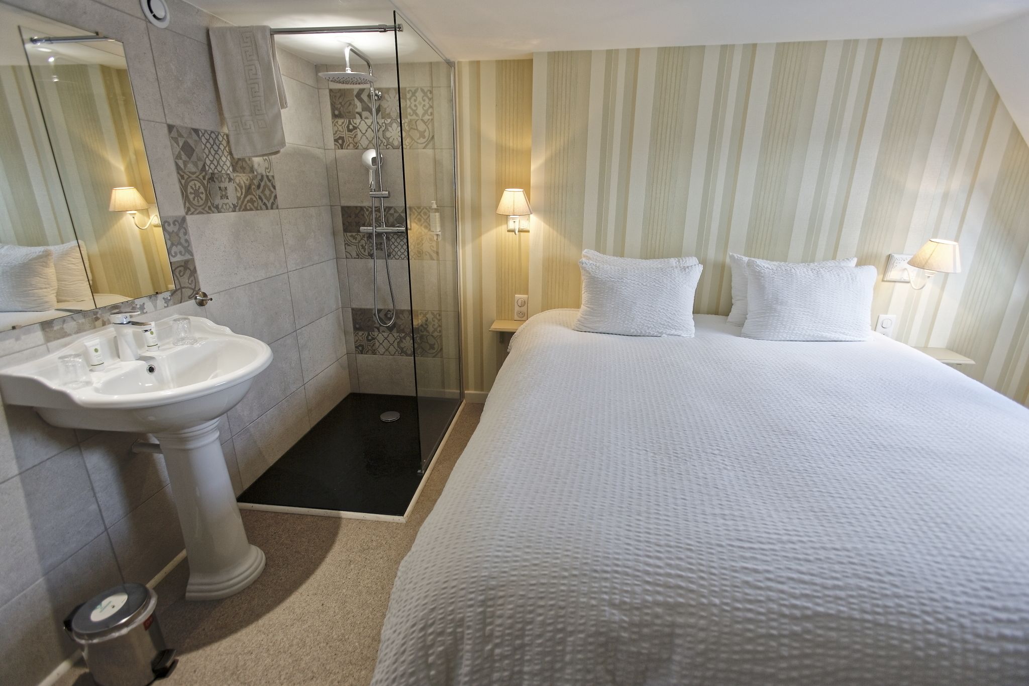 Una camera d'albergo con un letto grande, un bagno con lavandino e doccia, e carta da parati a righe.