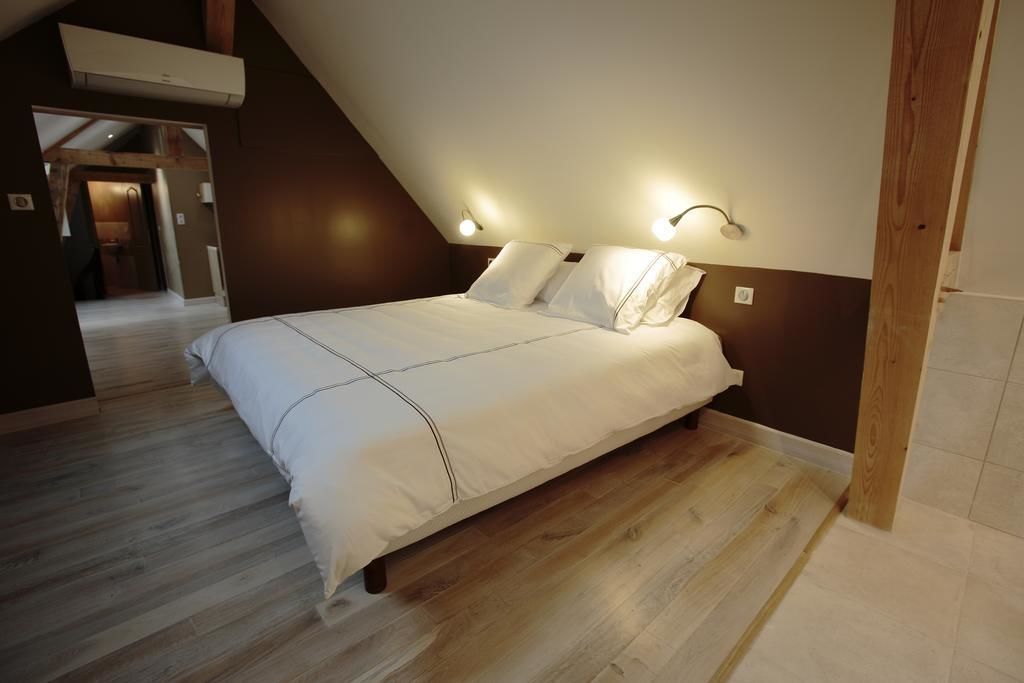 Ein Schlafzimmer mit schrägem Dach, Holzbalken, einem Bett mit weißer Bettwäsche und Wandleuchten.