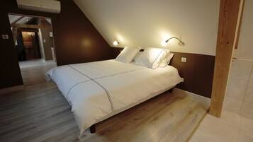 Ein Schlafzimmer mit schrägem Dach, Holzbalken, einem Bett mit weißer Bettwäsche und Wandleuchten.