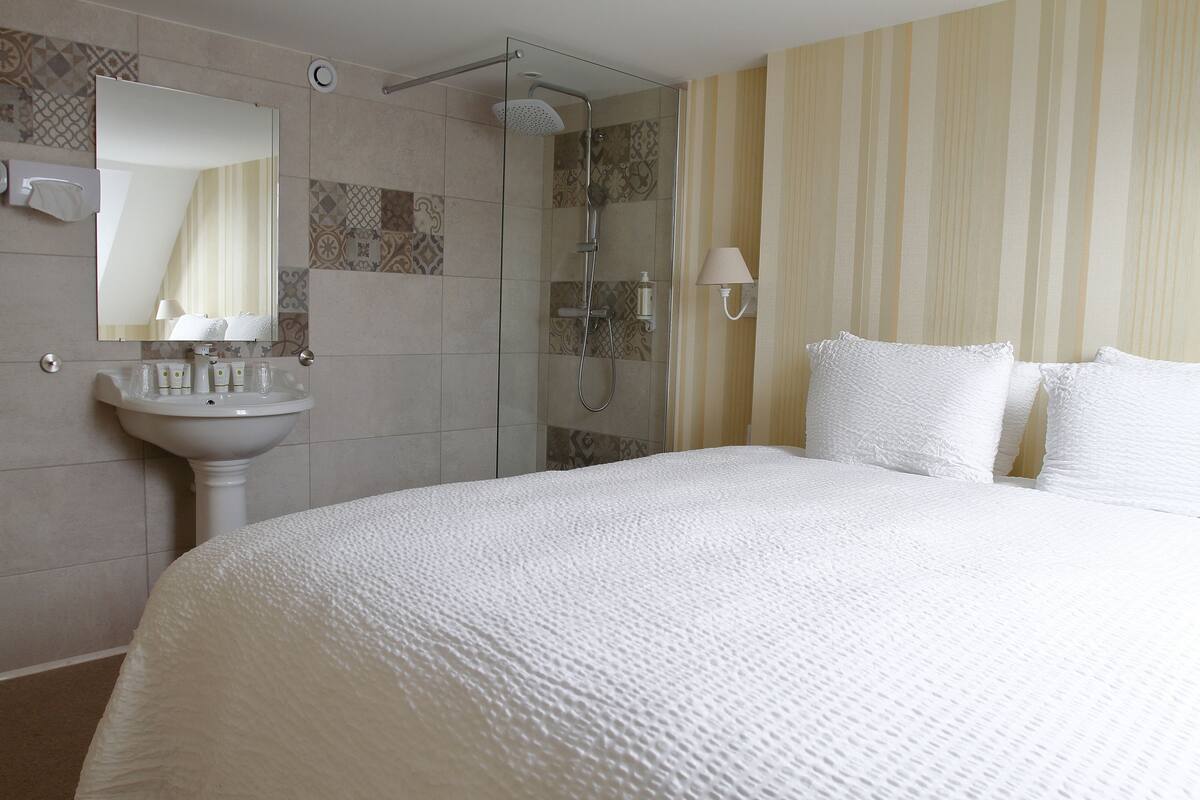 Een hotelkamer met een groot bed, een badkamer met douche, wastafel en spiegel.