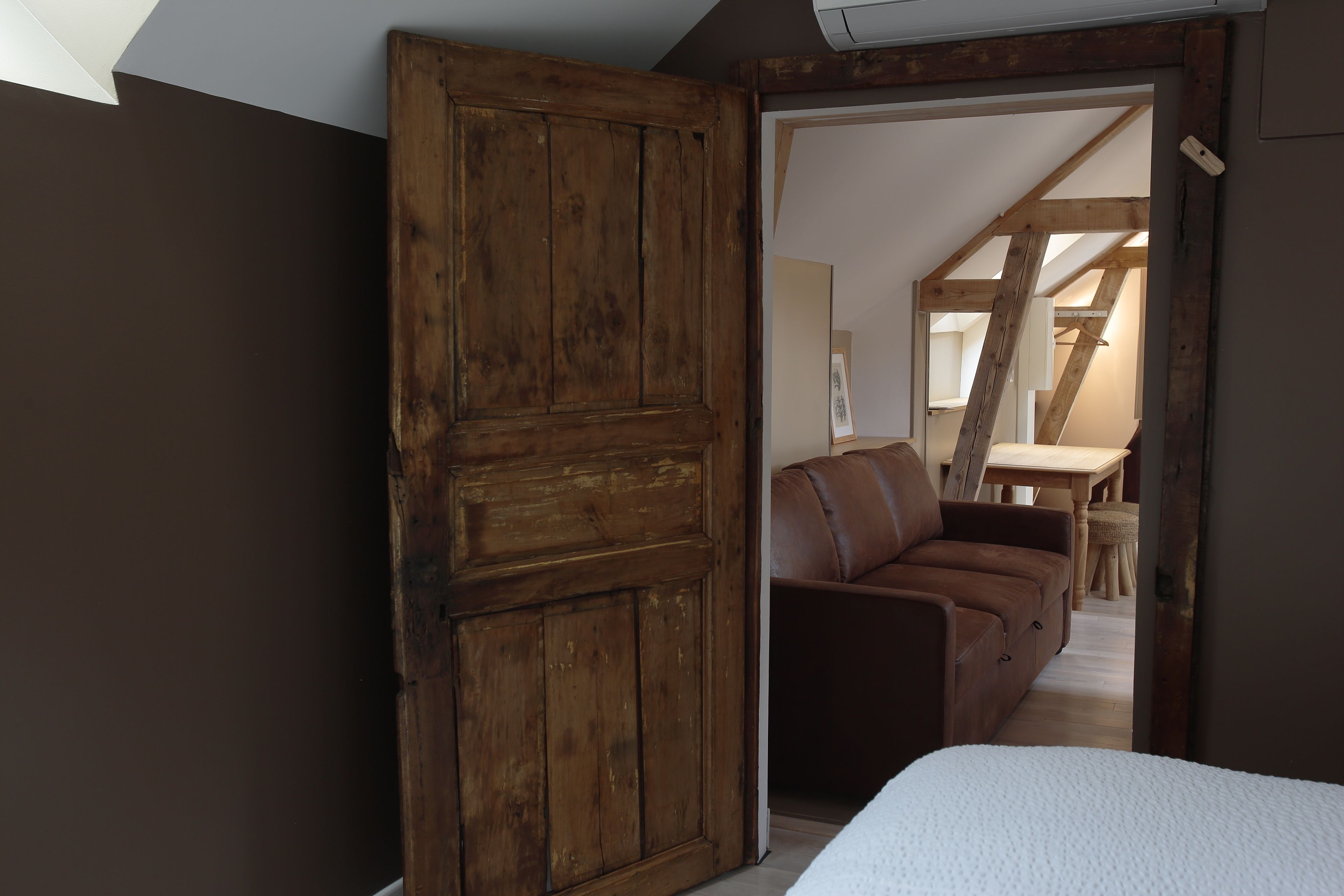 A room with a wooden door, a brown leather sofa, and a white bed.