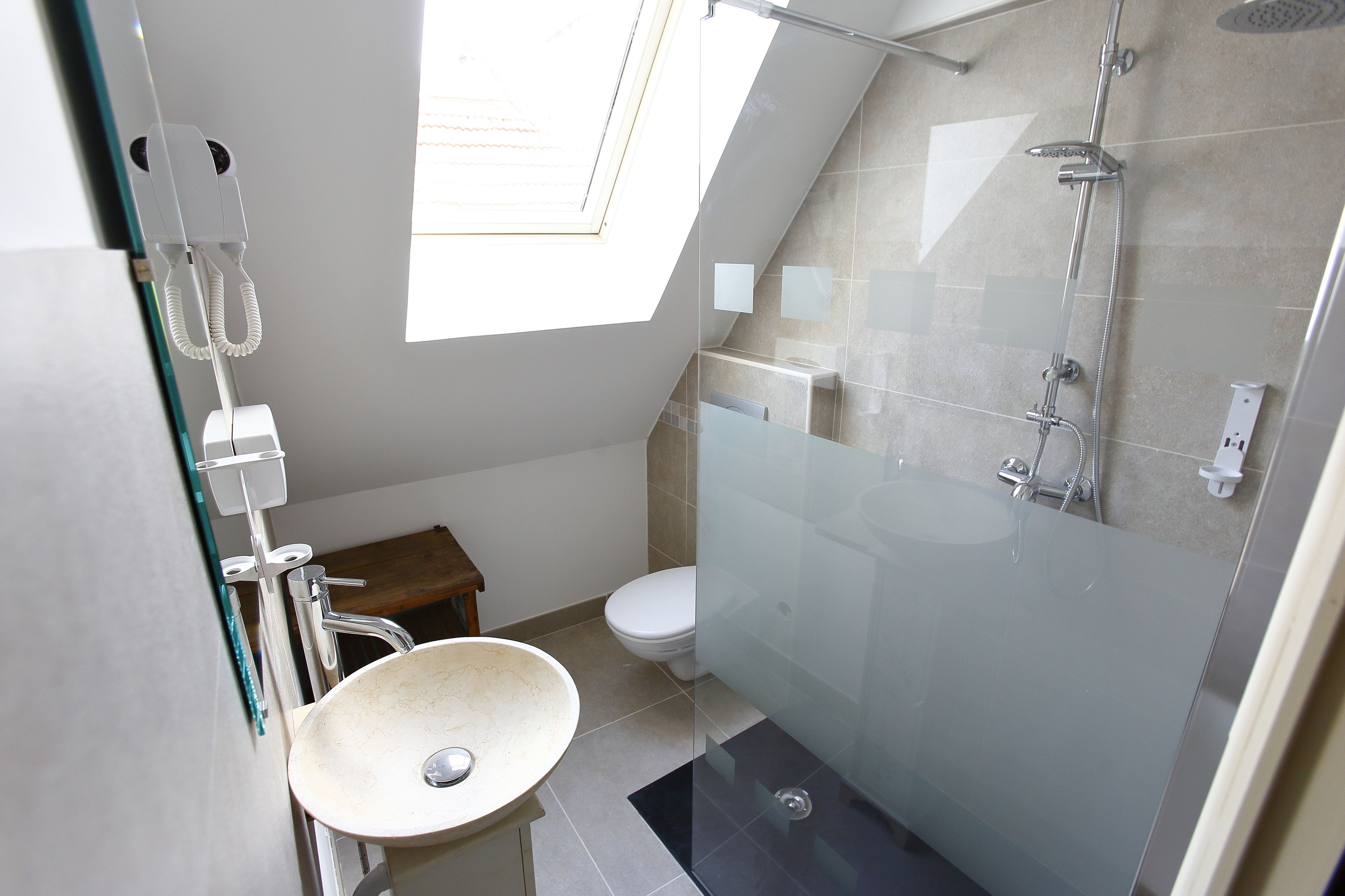 Un bagno moderno con una finestra a lucernario, un box doccia in vetro e un lavandino bianco.
