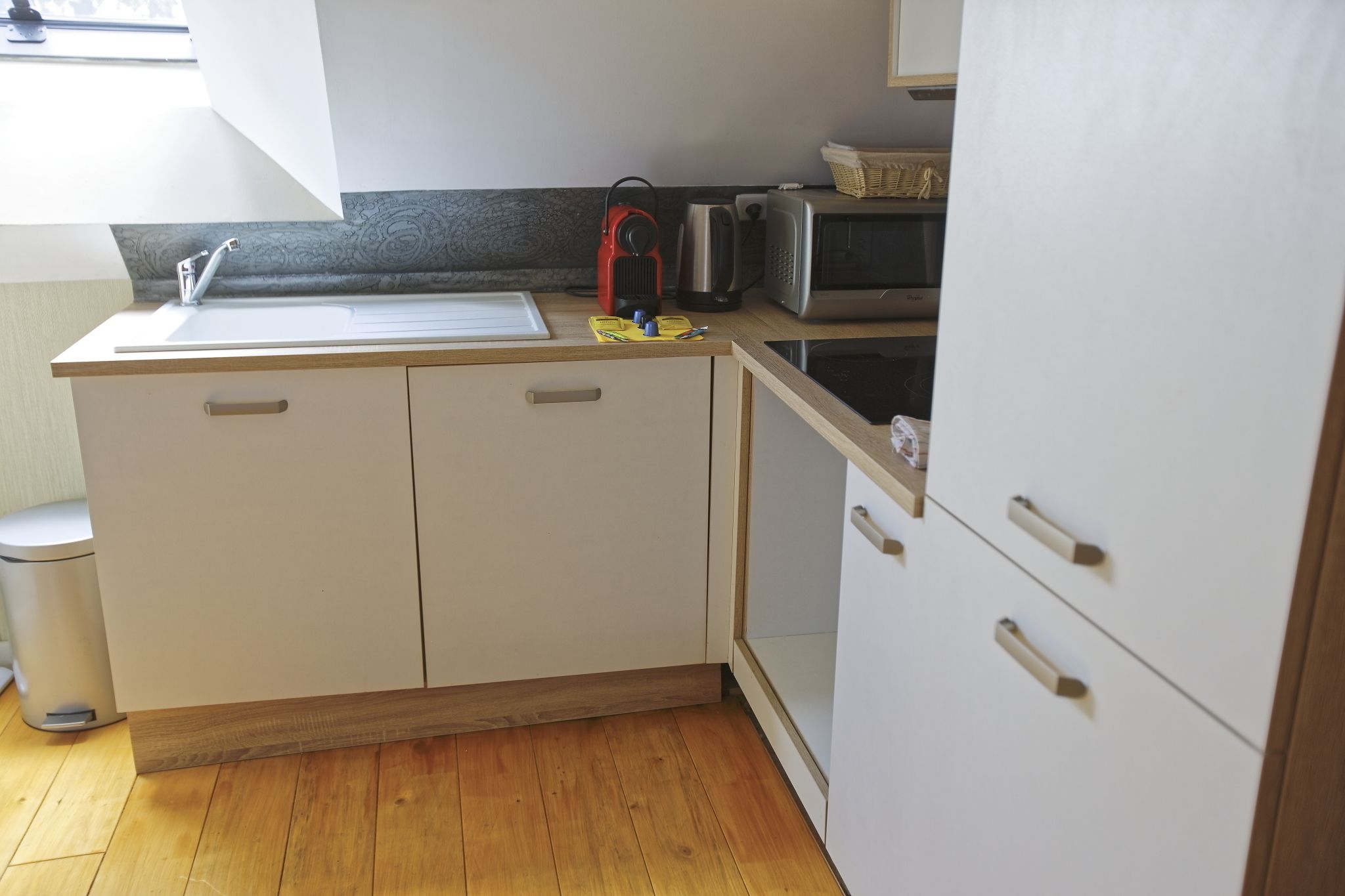 A compact kitchen with a sink, microwave, kettle, and a red portable heater.