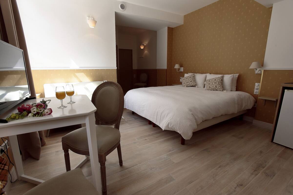 Een hotelkamer met een bed, een bureau met stoel, een televisie en een tafel met bloemen en glazen.