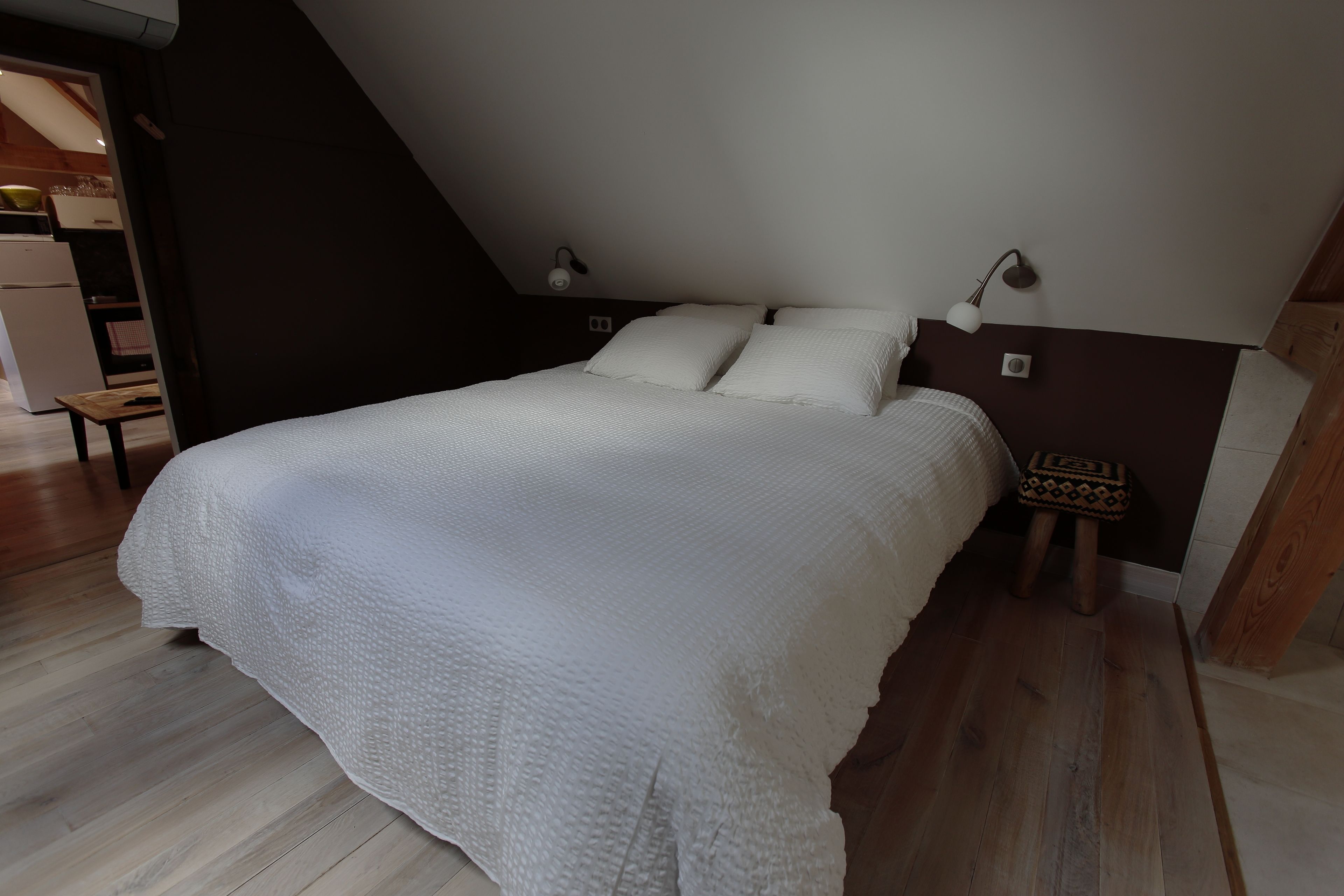 Et soveværelse med seng, et natbord, en lampe og en træskammel.