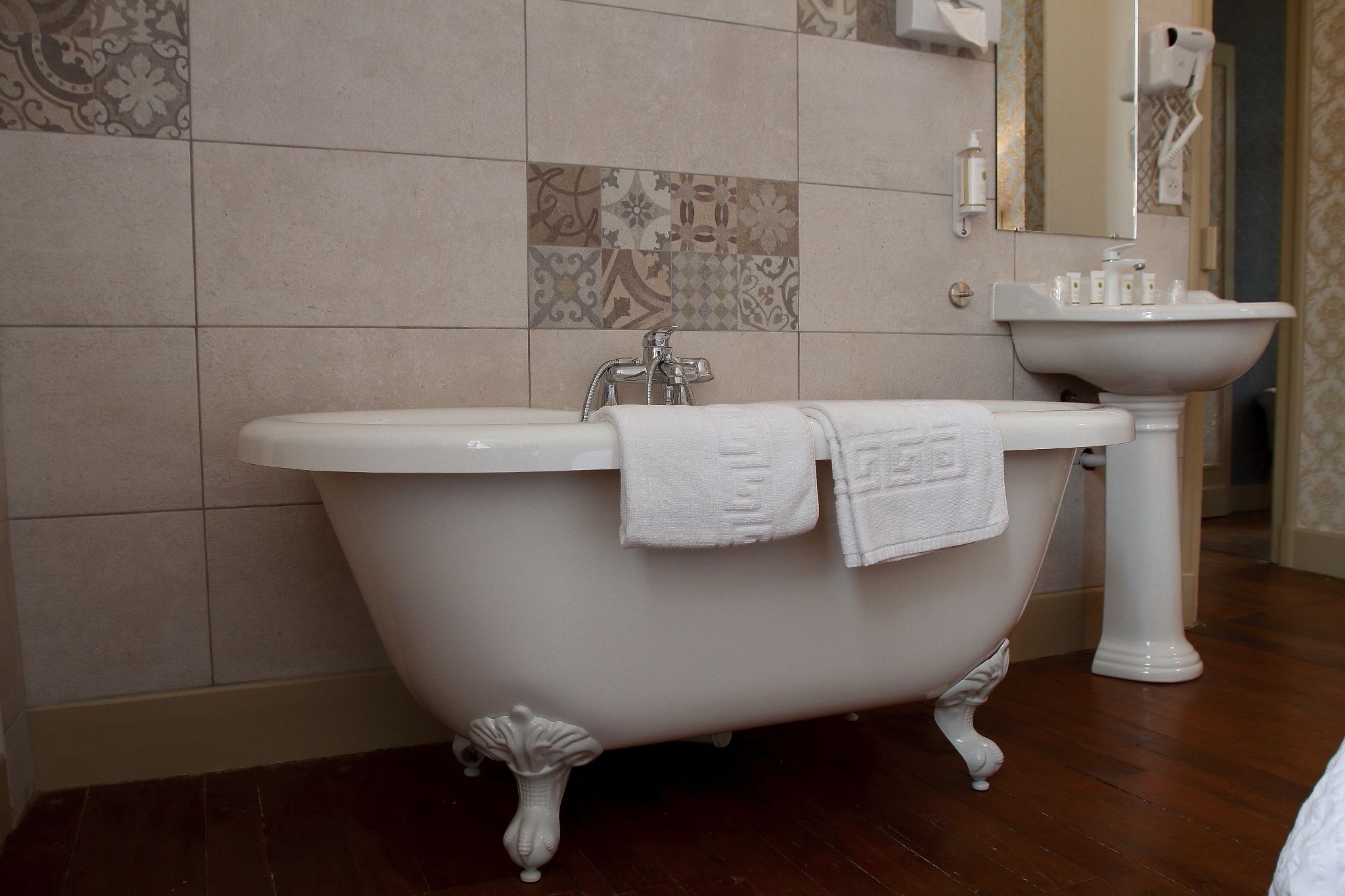 Une salle de bain avec une baignoire sur pieds, un lavabo sur colonne et des carreaux décoratifs aux murs.