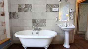 A bathroom with a freestanding bathtub, a pedestal sink, and a patterned tile wall.