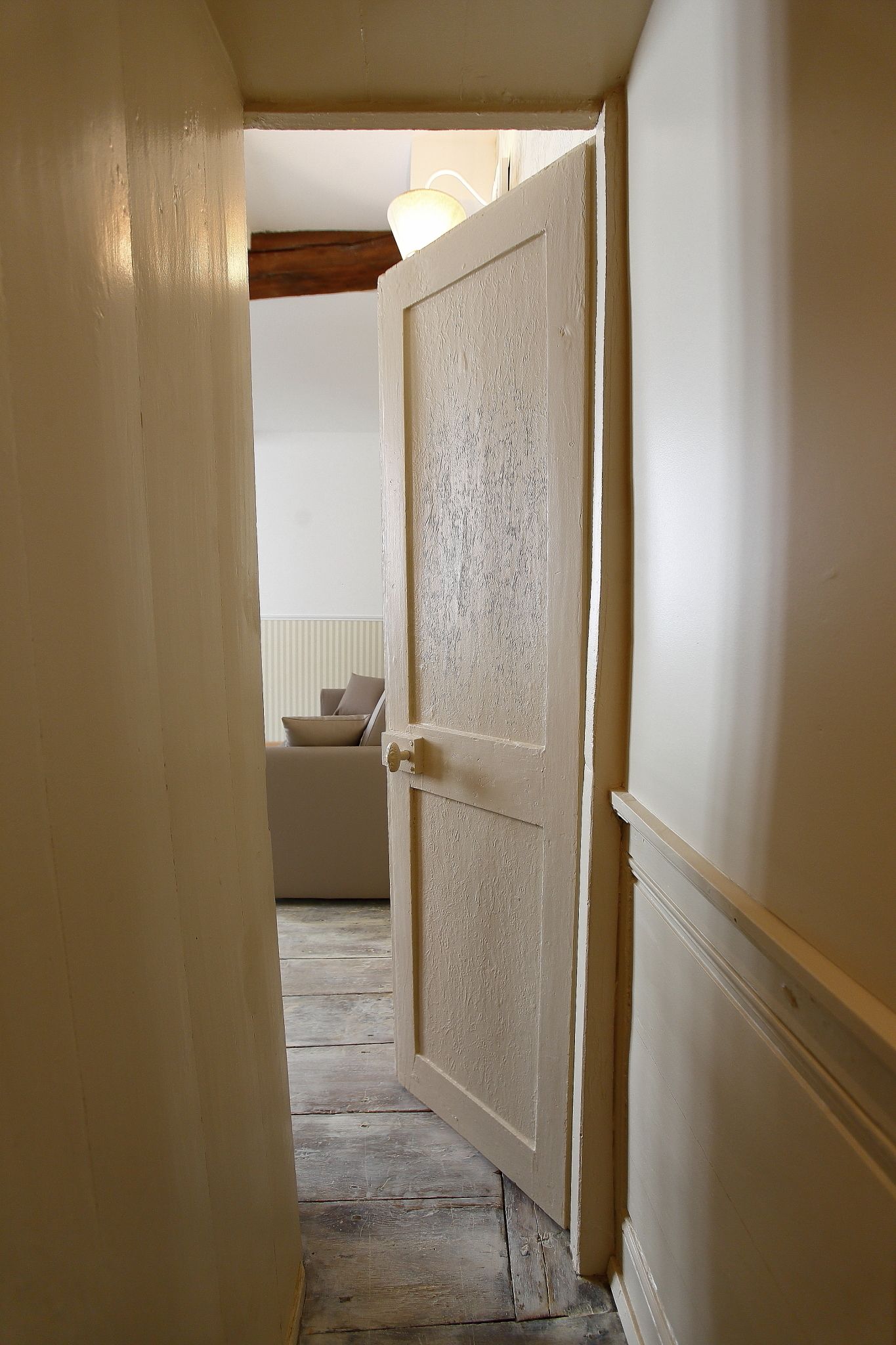 A hallway with a wooden floor leading to a room with a white door.