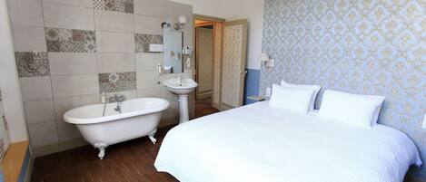 A bedroom with a large bed, a white bathtub, and a sink.