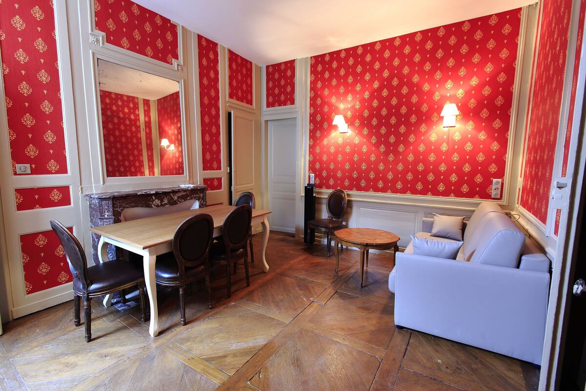 Een kamer met een eettafel en stoelen, een bank, een klein rond tafeltje en een spiegel.