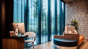 A modern reception area with a wooden desk, a laptop, a wicker chair, and a blue sofa. - The Originals Boutique, Hôtel Maison Montmartre Paris Les Puces (Paris)