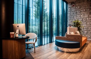 Una zona de recepción moderna con un escritorio de madera, una computadora portátil, una silla de mimbre y un sofá azul.