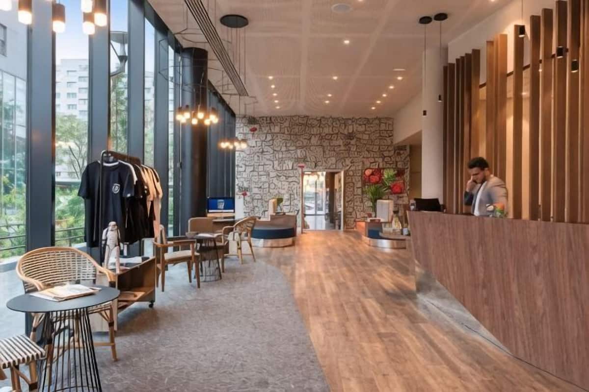 Un hall d’hôtel moderne avec un mur en pierre, un comptoir d’accueil en bois et un espace détente comprenant des chaises et des tables.