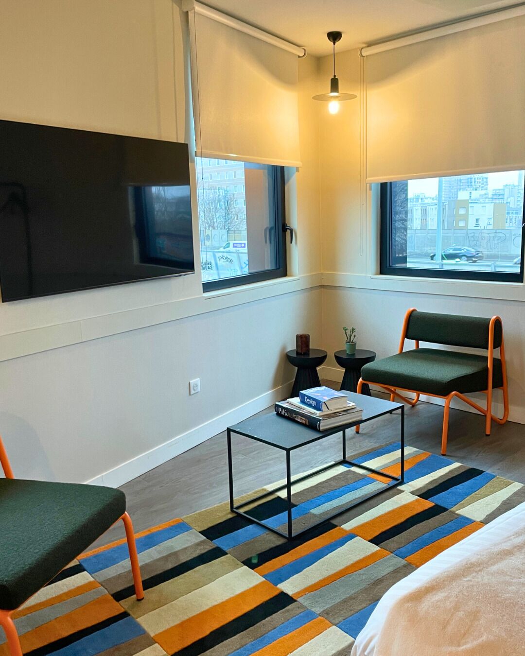 A modern room with a sofa, a small table with books, a coffee table, and a view through large windows.