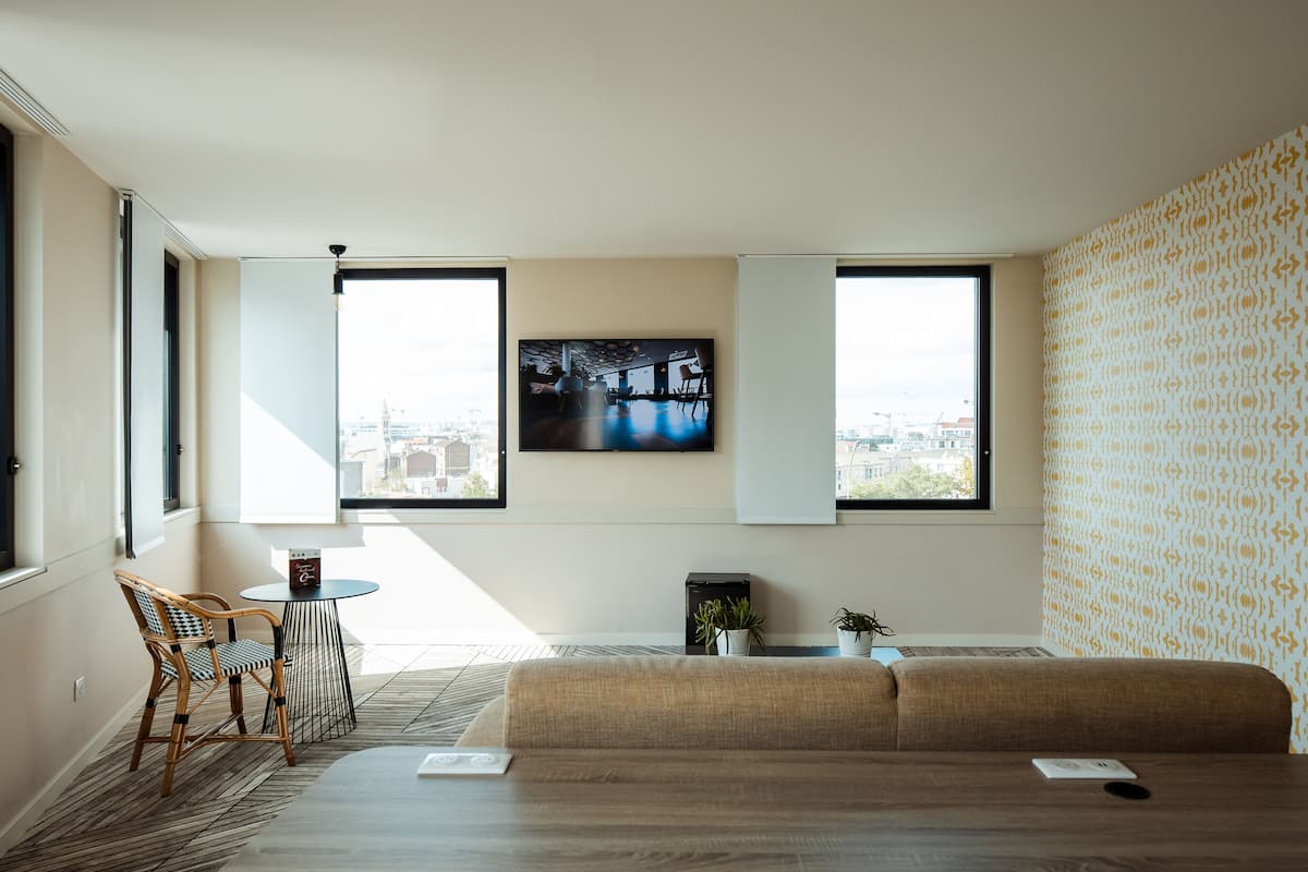 Un salon moderne avec un canapé, une petite table ronde, un fauteuil et un téléviseur fixé au mur.