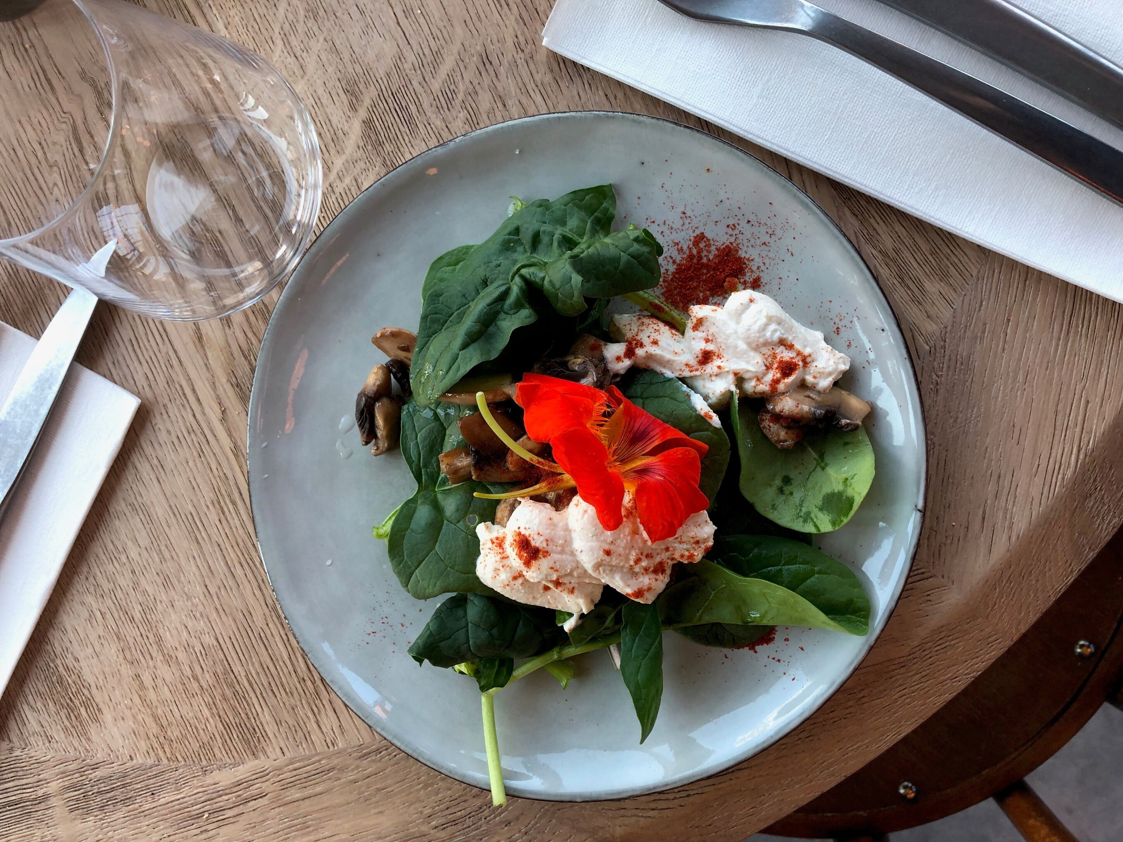 Une assiette contenant des épinards, des champignons et une fleur rouge, posée sur une table en bois.