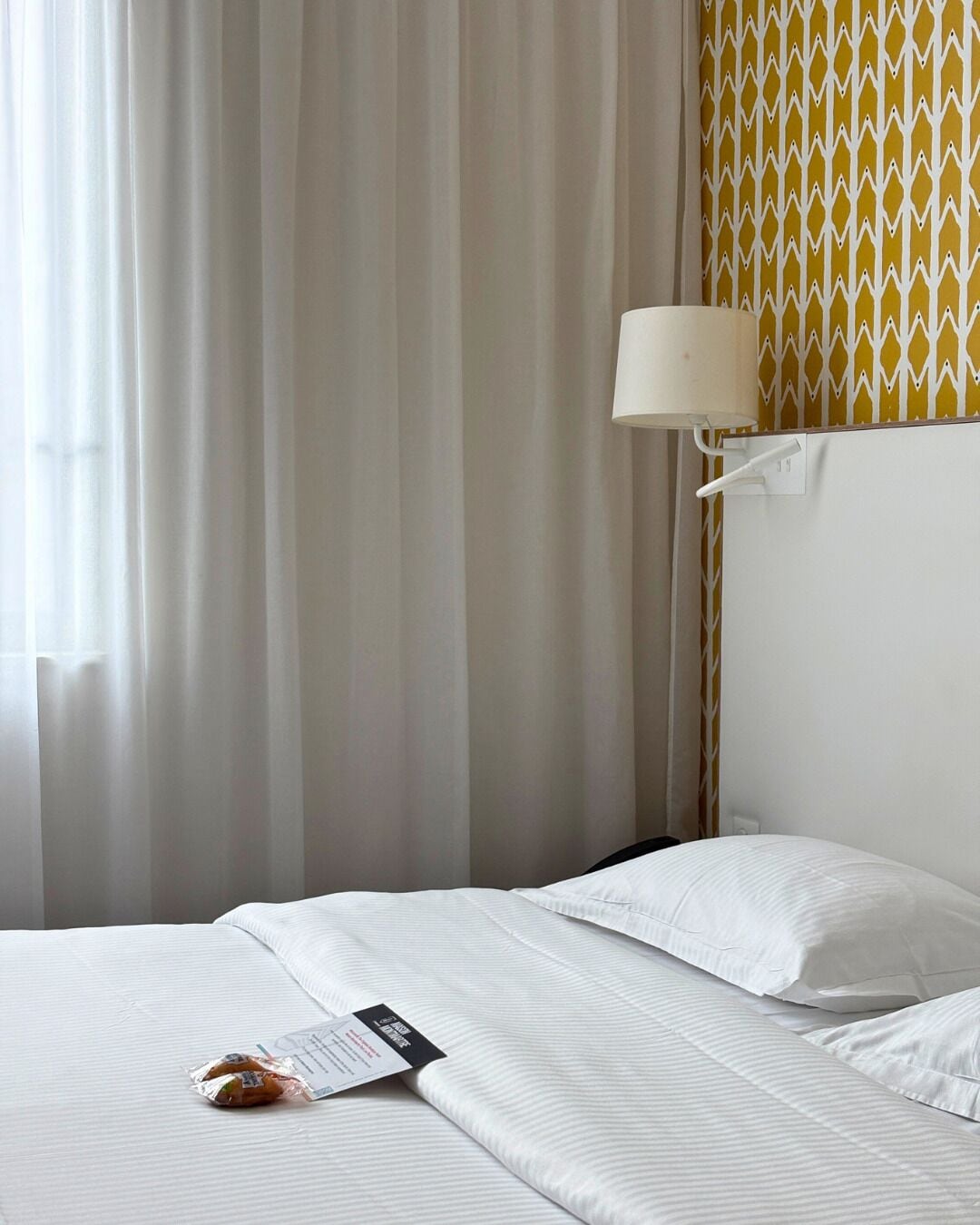 A hotel room with a bed, a lamp, and a patterned wall.