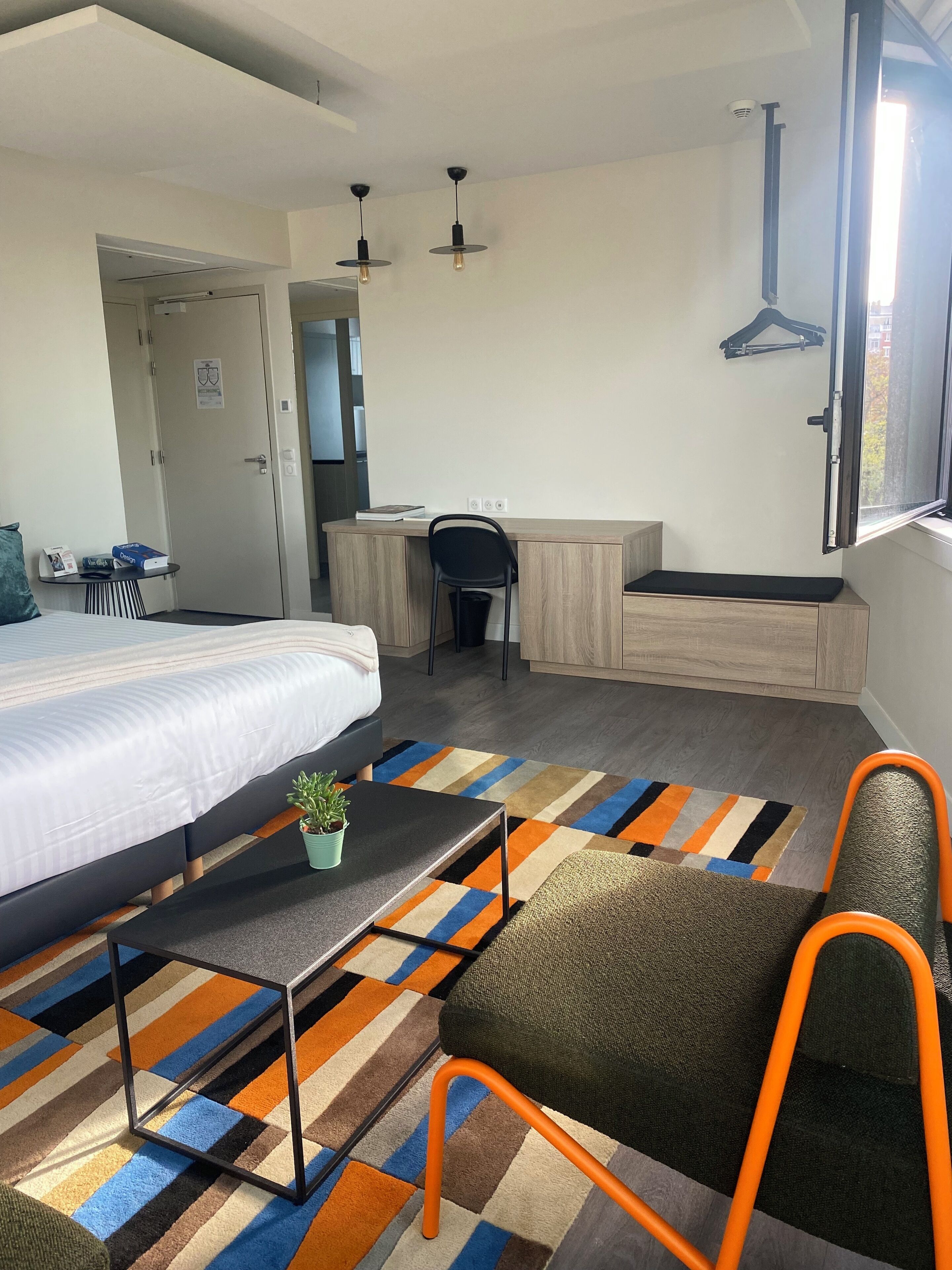 Una habitación de hotel con cama, escritorio, silla y una mesita con una planta.