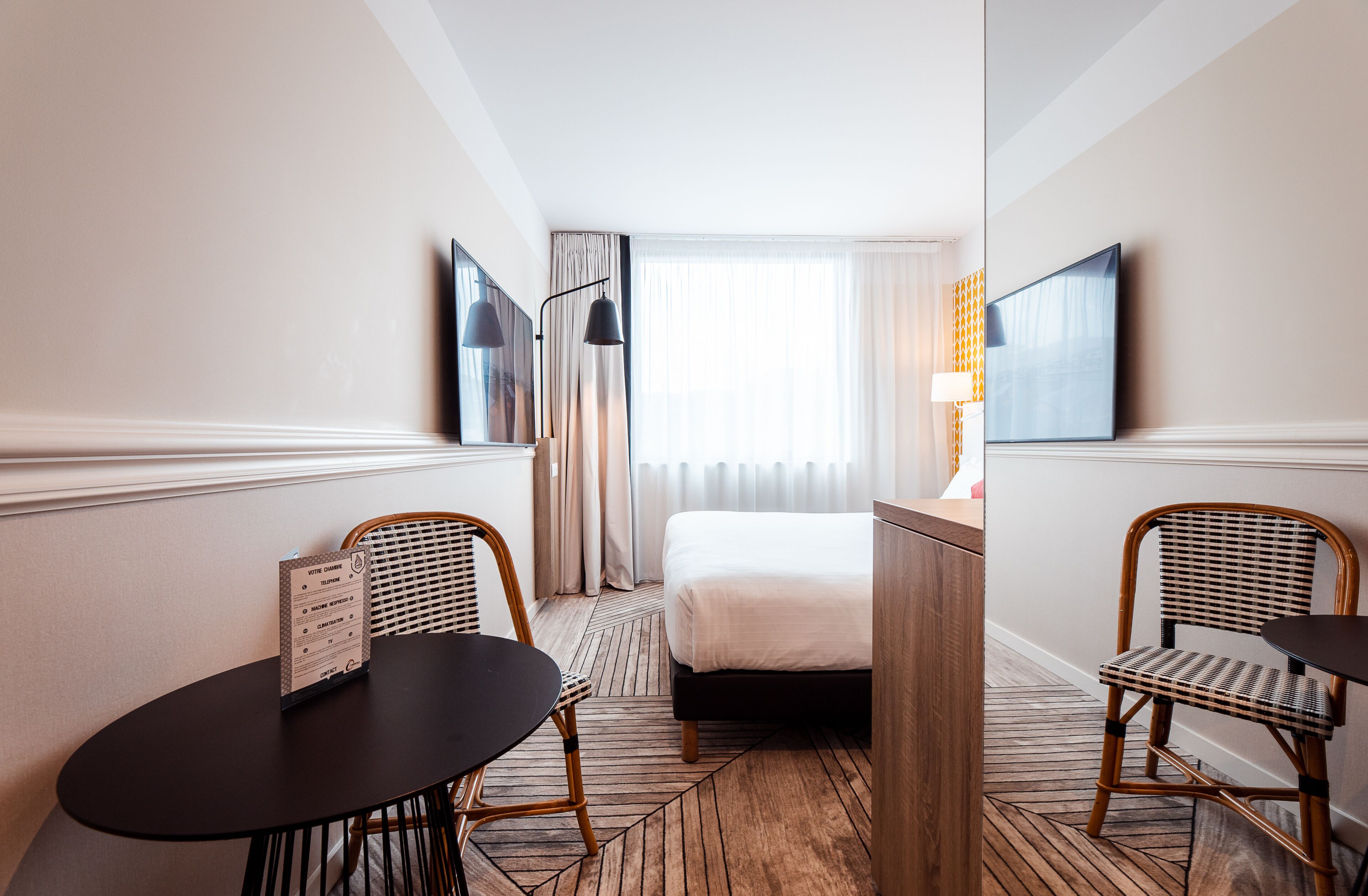 Ein Hotelzimmer mit einem Bett, einem Schreibtisch, zwei Stühlen, einem Fernseher und einem Vorhangfenster.