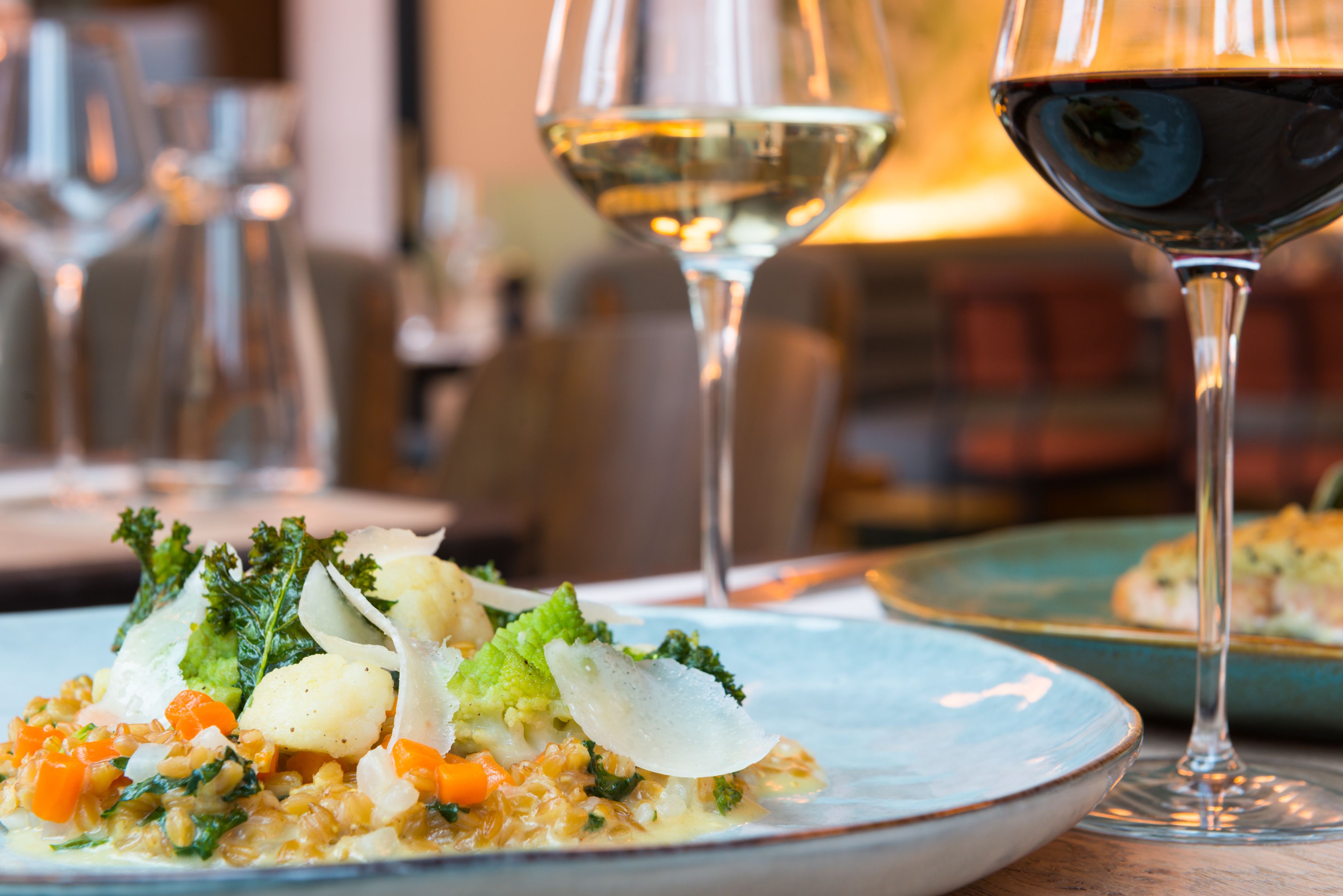A dining table with a plate of food, two wine glasses, and a blurred background.