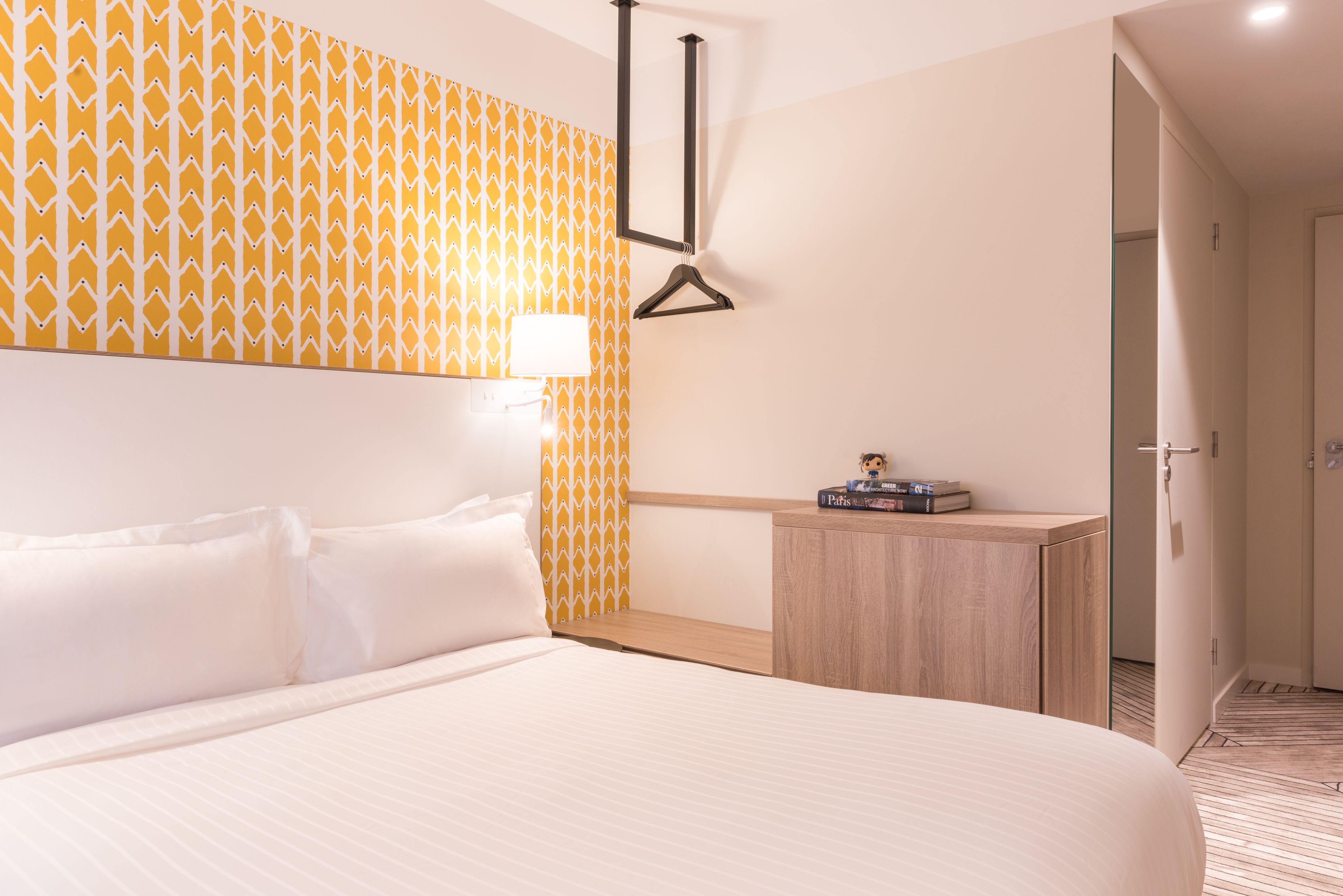Una habitación de hotel con una cama, una mesita de noche, una lámpara y una pared con un diseño geométrico.
