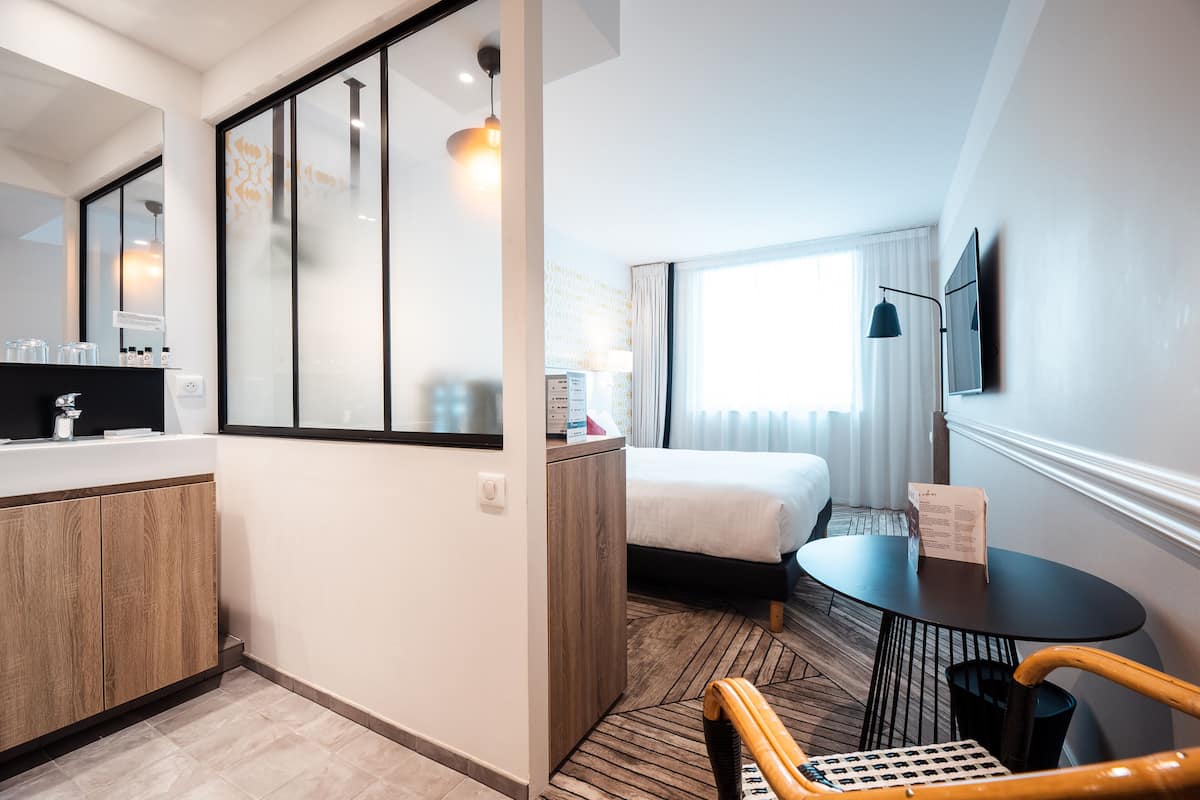 Une chambre d’hôtel moderne avec un meuble en bois, un lit, une table ronde et un téléviseur fixé au mur.