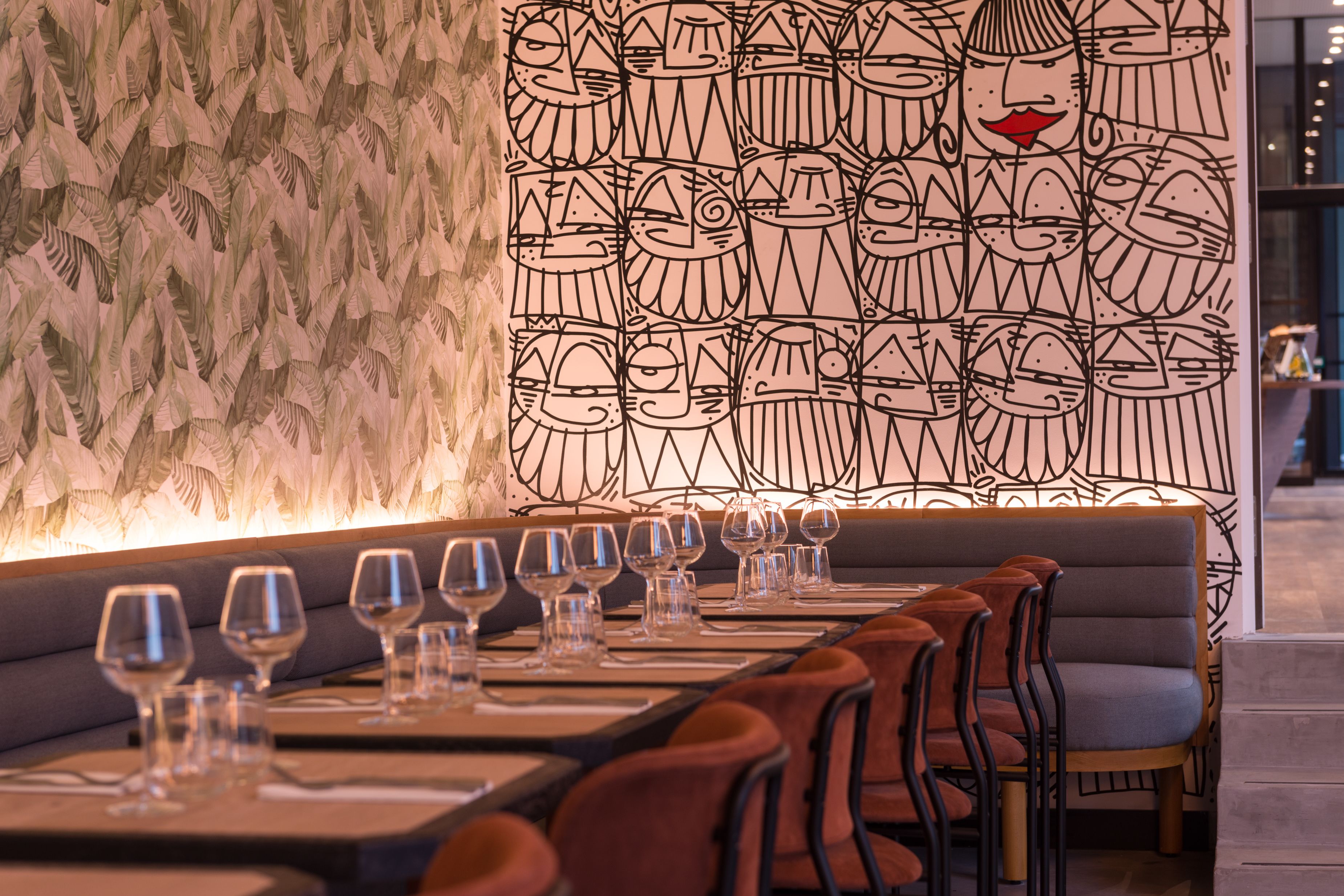 Un restaurante con una larga mesa de comedor dispuesta, con copas de vino vacías y sillas marrones.
