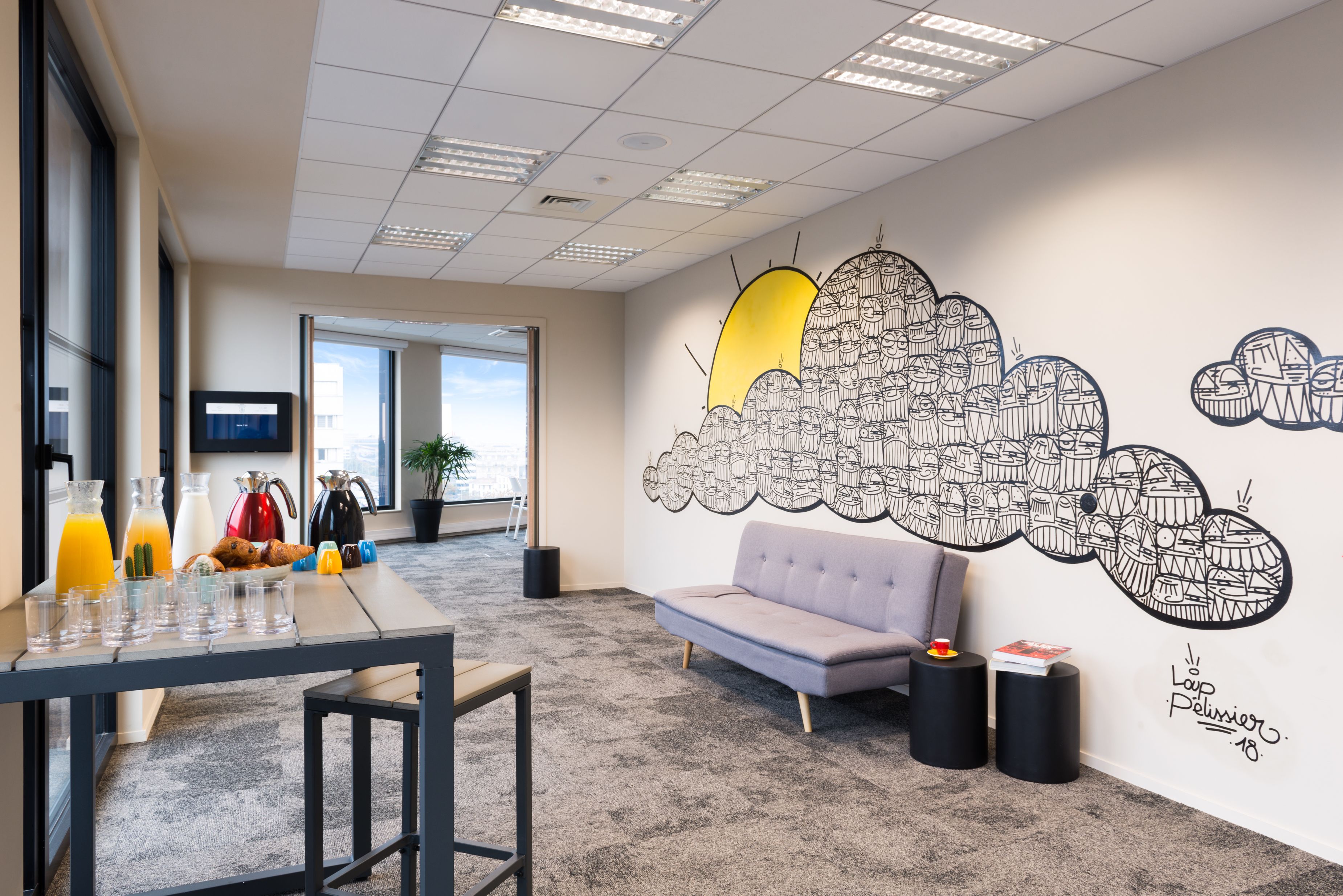 A modern office space with a long table, a sofa, and a wall mural.