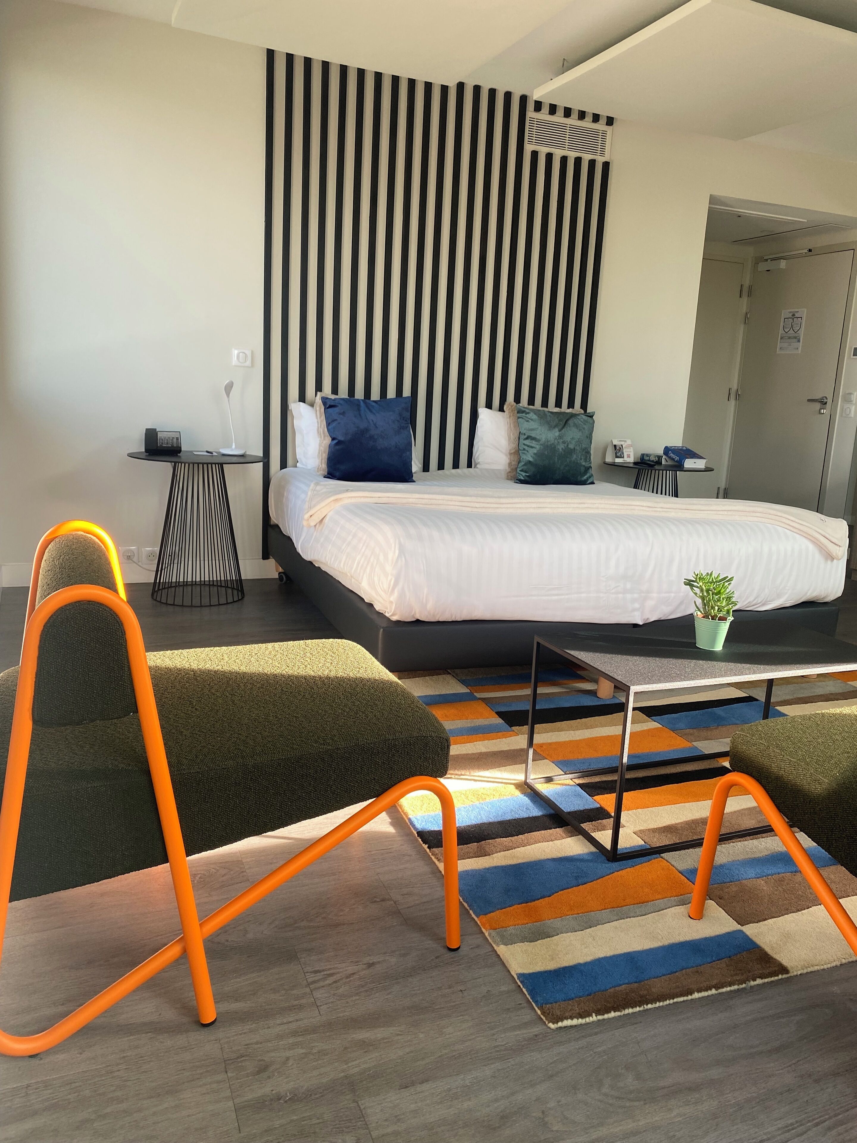 Een moderne hotelkamer met een groot bed, een klein nachtkastje, een stoel, een salontafel en een gestreepte wand.