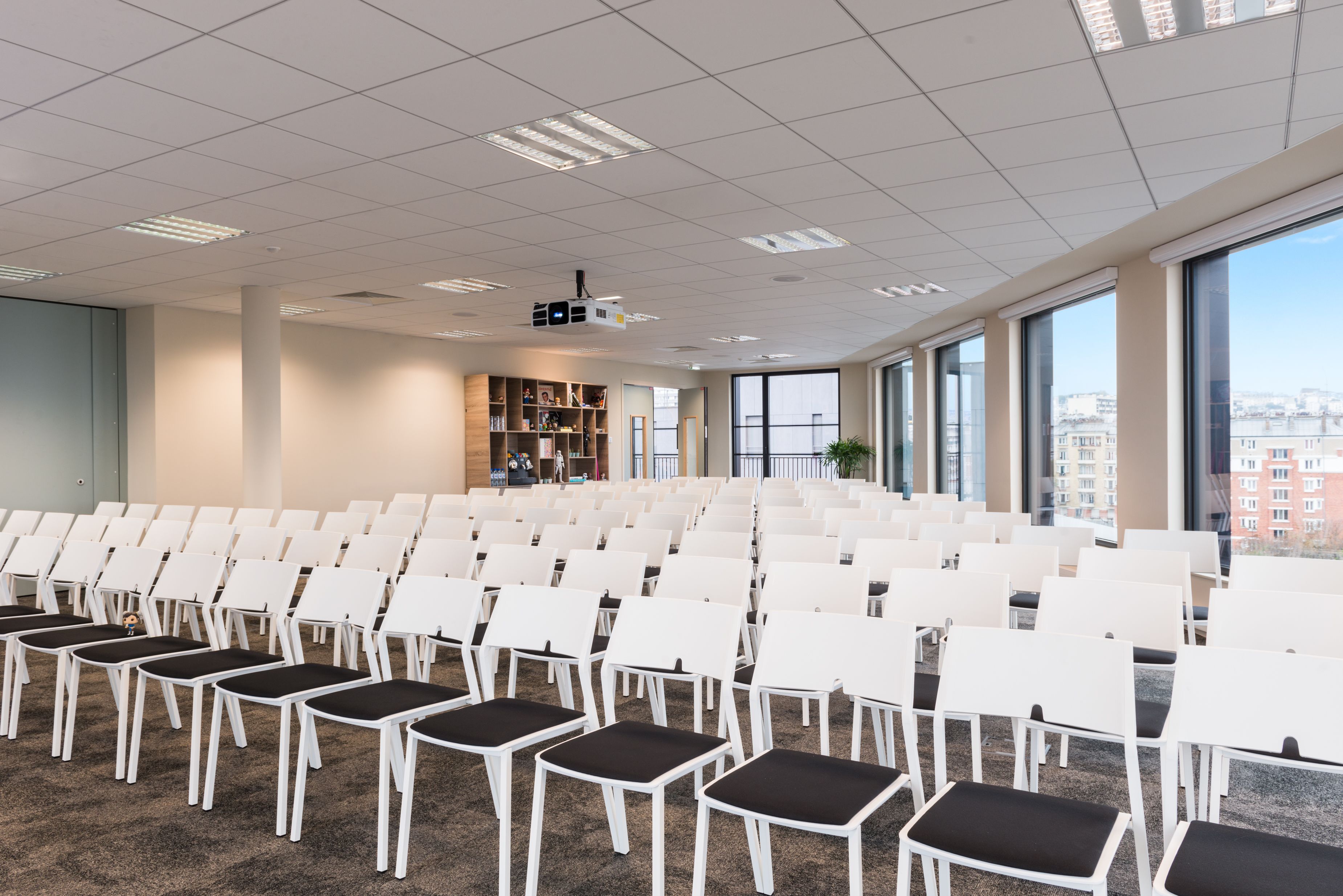 Une salle de conférence avec des rangées de chaises blanches et un écran de projection.