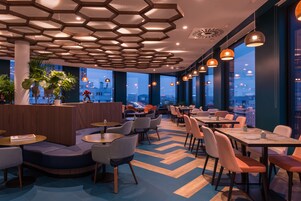 Un restaurante moderno con luces de techo hexagonales, mesas y sillas redondas.