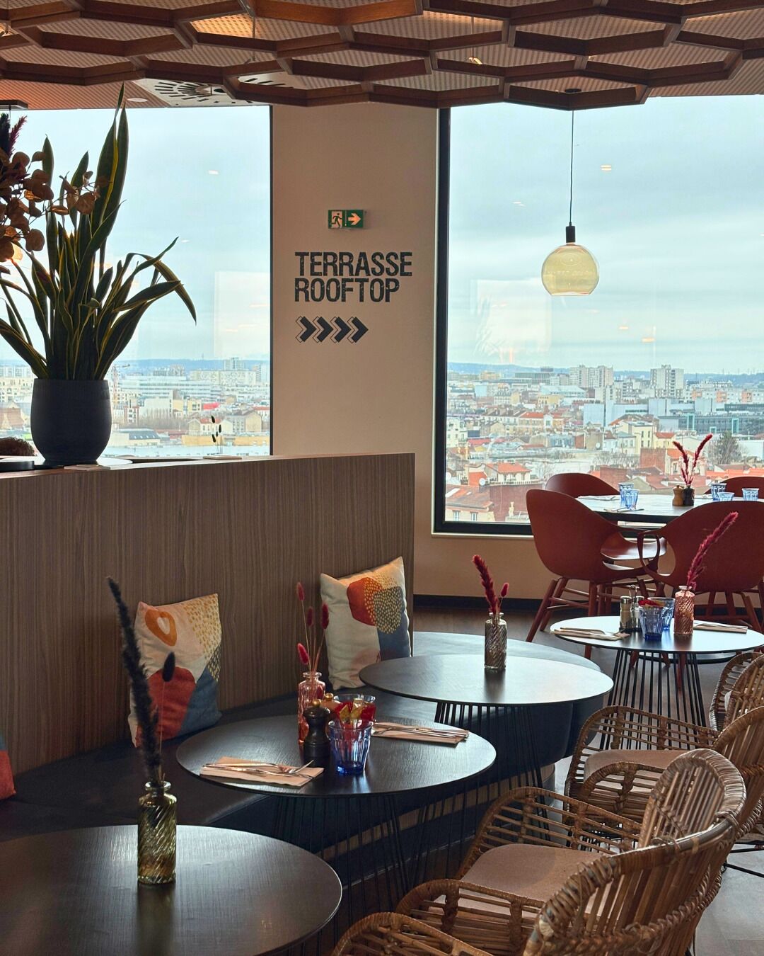 A restaurant with a terrace rooftop view, seating arrangements, and a cityscape in the background.