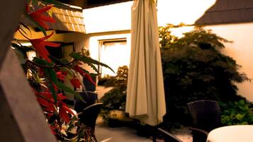 An outdoor patio area with a table and chairs, a hanging umbrella, and potted plants.